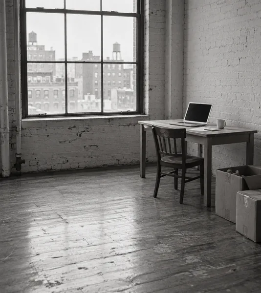 An empty Brooklyn loft in 2012: one desk, a laptop and moving boxes by a tall window